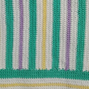 Puede incluir: Primer plano de una tela de crochet con rayas de hilo verde, blanco, morado y amarillo.