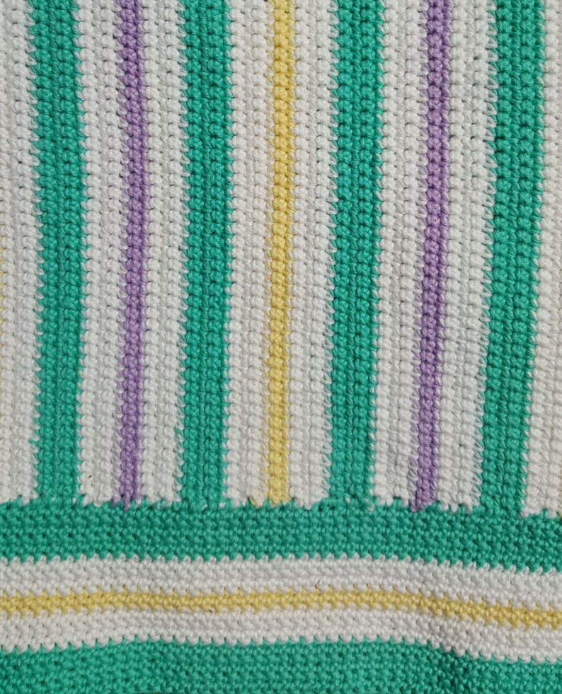 Puede incluir: Primer plano de una tela de crochet con rayas de hilo verde, blanco, morado y amarillo.