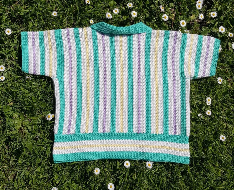 Puede incluir: Un top de crochet a rayas con cuello, mangas cortas y un patr&oacute;n de rayas blancas, amarillas y moradas sobre un fondo azul verdoso.