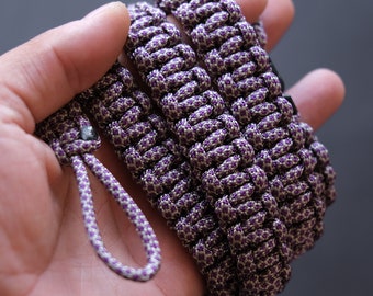Op de afbeelding: Een paars en wit gevlochten koord met een lus aan het ene uiteinde. Het koord is gemaakt van een dik, duurzaam materiaal en is perfect voor knutselen of het maken van sieraden.
