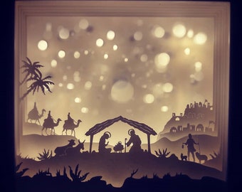 May include: A paper cut-out nativity scene with a starlit sky, a stable, three wise men riding camels, a donkey, a sheep, and a shepherd with a staff and a dog.
