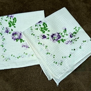 May include: Two white cotton handkerchiefs with a purple and green floral pattern. The handkerchiefs have a grid pattern.