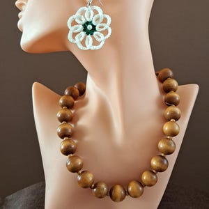Peut inclure: Un collier, un bracelet et des boucles d'oreilles en crochet blanc avec des accents verts. Le collier est fait de perles en bois.