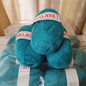 Può includere: Un gruppo di gomitoli di filato color turchese in un sacchetto di plastica trasparente. Ogni gomitolo ha un'etichetta bianca con la scritta "MALAYA" in rosso. Il filato è morbido e soffice, perfetto per progetti di maglieria o uncinetto.