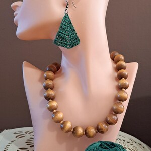 May include: A green crocheted necklace with wooden beads, a matching pair of earrings, a ball of green yarn, and a crochet hook.
