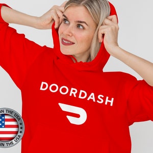 Op de afbeelding: Rood hoodie met de witte tekst "DOORDASH" en een wit gestileerd "D" logo. De hoodie heeft een "MADE IN THE USA" label.