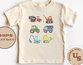May include: A beige short-sleeved t-shirt with a watercolor illustration of construction vehicles. The vehicles include a cement mixer, a crane, a tractor, a dump truck, an excavator, and a bulldozer.