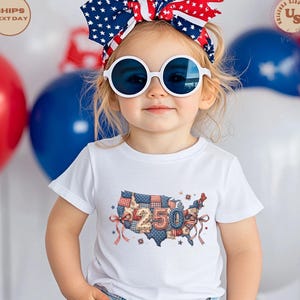 Op de afbeelding: Een kind draagt een wit T-shirt met een kleurrijke kaart van de Verenigde Staten met het nummer "250". Het ontwerp is versierd met sterren en linten. Het kind draagt ook een patriottische hoofdband en een ronde zonnebril.