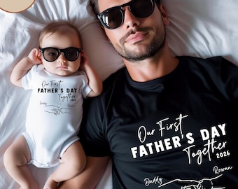 May include: A black t-shirt and a white baby onesie with matching text that reads "Our First Father's Day Together 2026". The text is in a script font with a graphic of two hands holding each other. Both the man and baby are wearing sunglasses.