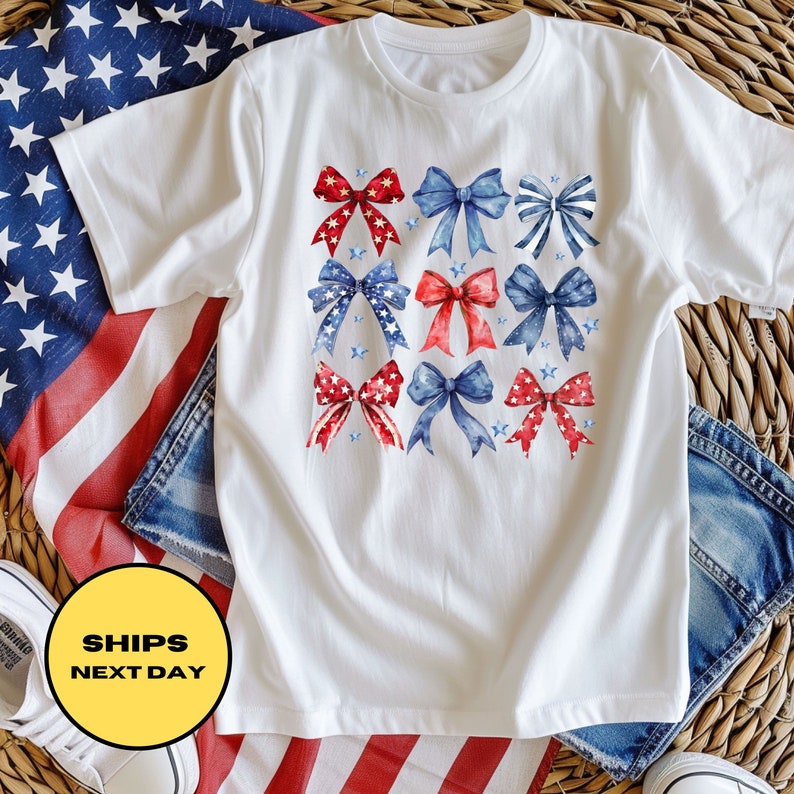 May include: White t-shirt with a red, white, and blue bow design. The bows are arranged in a grid pattern and have a watercolor effect. The shirt is a great way to show your patriotic pride.