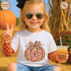 Puede incluir: Una ni&ntilde;a lleva una camiseta blanca con un dise&ntilde;o de calabaza floral y mangas de lunares naranjas. La ni&ntilde;a sostiene una bebida que dice "Take Me To The Pumpkin Patch". El fondo incluye una calabaza grande y heno.