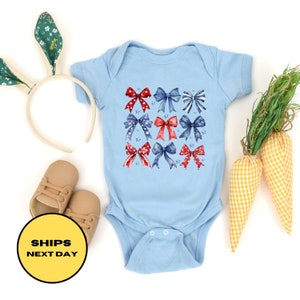 May include: A light blue baby onesie with a pattern of red, white, and blue bows. The bows are arranged in a grid pattern and have a watercolor effect.