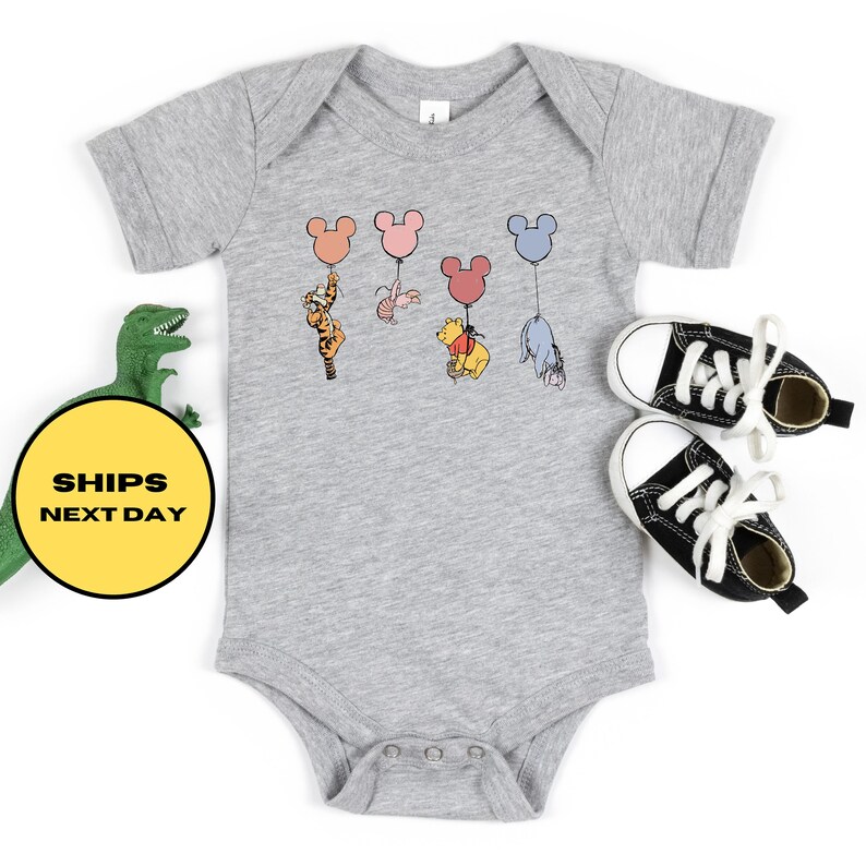 May include: A gray baby onesie with a graphic of Winnie the Pooh, Tigger, Piglet, Eeyore, and a rabbit holding onto colorful Mickey Mouse balloons.