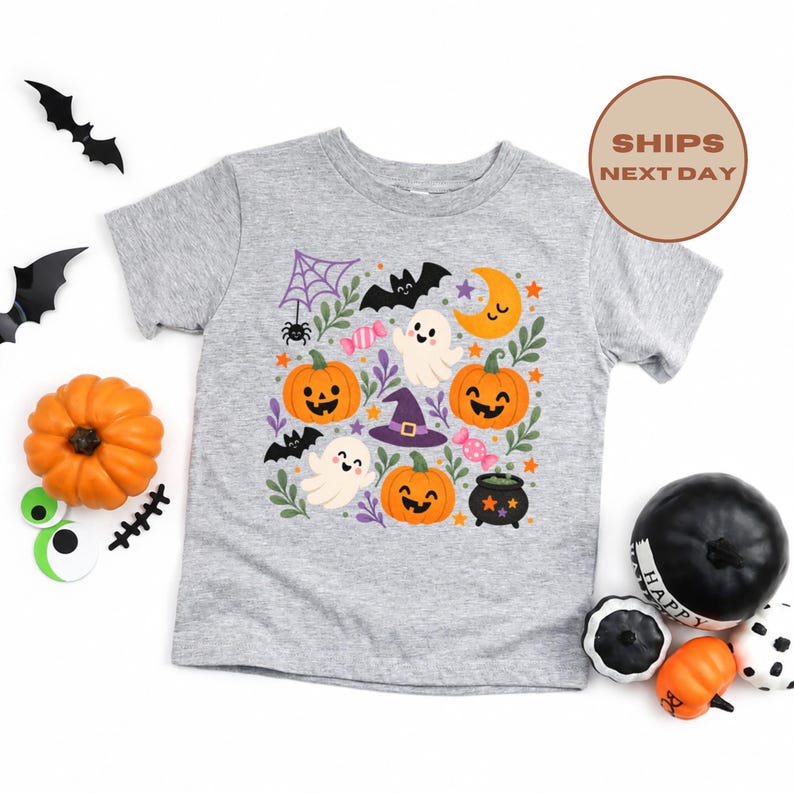 Puede incluir: Una camiseta gris jaspeado de manga corta con un estampado gr&aacute;fico colorido de tem&aacute;tica de Halloween. El dise&ntilde;o incluye calabazas sonrientes, fantasmas blancos, un sombrero de bruja morado, un murci&eacute;lago negro, una telara&ntilde;a, una luna y dulces.