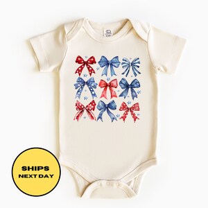 May include: A cream-colored baby onesie with a pattern of red and blue bows and stars.