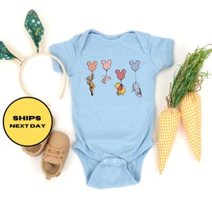 May include: A light blue baby onesie with a graphic of Winnie the Pooh, Tigger, Piglet, and Eeyore holding onto colorful Mickey Mouse balloons.