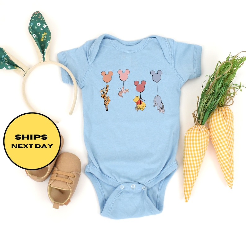 May include: A light blue baby onesie with a graphic of Winnie the Pooh, Tigger, Piglet, and Eeyore holding onto colorful Mickey Mouse balloons.