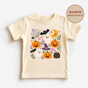 Puede incluir: Una camiseta de manga corta color crema con un estampado gr&aacute;fico colorido con tem&aacute;tica de Halloween. El dise&ntilde;o incluye calabazas naranjas, fantasmas blancos, un sombrero de bruja morado, una ara&ntilde;a negra con telara&ntilde;a, murci&eacute;lagos y dulces.