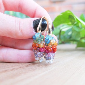 May include: Rainbow gemstone earrings with gold hoops. The earrings feature a cascade of colourful gemstones, including blue topaz, green peridot, yellow citrine, orange carnelian, red ruby, purple amethyst, and blue sapphire.