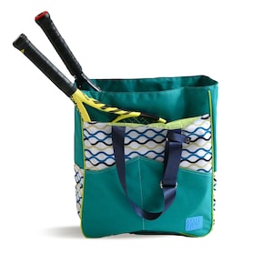Puede incluir: Una bolsa de lona azul turquesa con ribete verde y un patrón ondulado azul y blanco en el bolsillo delantero. Dos raquetas de tenis amarillas y negras sobresalen de la parte superior de la bolsa. La bolsa tiene una correa azul y una pequeña etiqueta azul que dice "Easy Win".