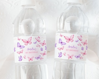 Könnte beinhalten: Zwei durchsichtige Plastikwasserflaschen mit personalisierten Etiketten, die ein Aquarell-Schmetterlingsdesign zeigen. Die Etiketten sind rosa und lila mit dem Text "Amelia's 1st Birthday".