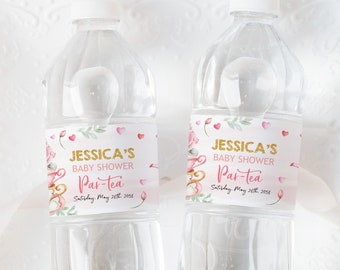 Puede incluir: Dos botellas de agua de plástico transparente con etiquetas rosas y doradas que dicen "Jessica's Baby Shower Par-tea" con una fecha. Las etiquetas tienen un diseño floral de acuarela.