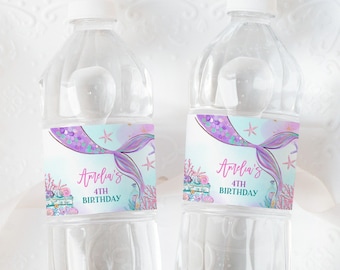 Op de afbeelding: Twee doorzichtige plastic waterflessen met etiketten met een zeemeerminstaart, schelpen en de tekst "Amelia's 4th Birthday".