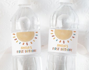 Puede incluir: Dos botellas de agua de plástico transparente con etiquetas personalizadas. Las etiquetas presentan un sol amarillo con acentos naranja, rojo, azul y verde. El texto en las etiquetas dice "Amelia's First Birthday".