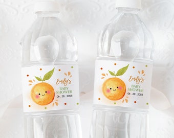 May include: Two clear plastic water bottles with orange and green labels. The labels feature a cartoon orange with a smiling face and the text "Emily's Baby Shower 09.28.2023".