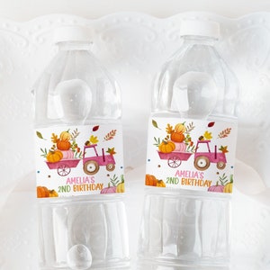 May include: Two clear plastic water bottles with labels featuring a pink tractor carrying pumpkins and fall leaves. The labels also say "Amelia's 2nd Birthday".