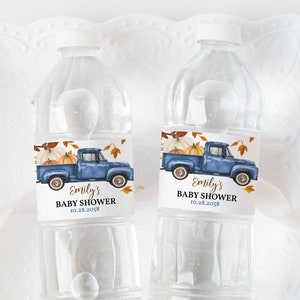 May include: Two clear plastic water bottles with labels featuring a blue pickup truck carrying pumpkins and fall leaves. The labels also include the text "Emily's Baby Shower 10.28.2028".