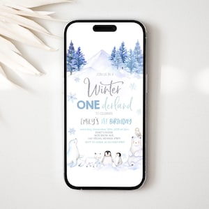 May include: A blue and white winter wonderland themed first birthday party invitation with a snowy mountain scene and woodland animals. The text reads "Join us in a Winter Wonderland to celebrate Emily's 1st Birthday".