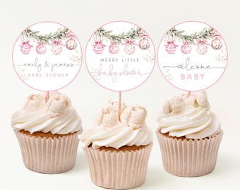 May include: Three cupcakes with white icing and pink toppers. The toppers are circular, featuring pink and white baubles, foliage, and text saying "emily & james's baby shower", "merry little baby shower", and "welcome baby".