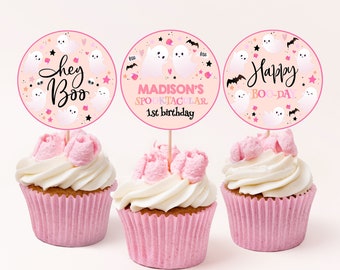 Op de afbeelding: Drie roze cupcakes met witte frosting en cupcake-toppers met een spookthema. De toppers zijn roze en wit met de tekst "Hey Boo", "Madison's Spooktacular 1st birthday" en "Happy Boo-Day".