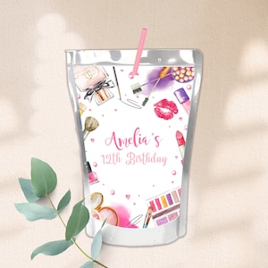 May include: A white juice pouch with a pink straw and a design of makeup items, including lipstick, eyeshadow, and perfume bottles. The text "Amelia's 12th Birthday" is printed on the pouch.