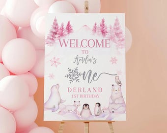 May include: Welcome to Amelia's One Derland 1st Birthday sign with a pink and white winter wonderland theme. The sign features a polar bear, a seal, and penguins.