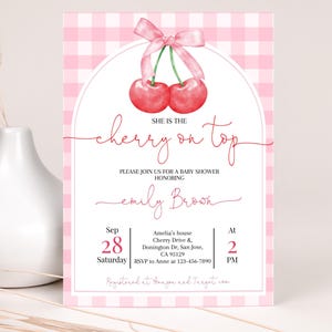 Może przedstawiać: Różowe i białe zaproszenie na baby shower w kratkę z akwarelową ilustracją dwóch czerwonych wiśni z zielonymi szypułkami i liśćmi. Tekst brzmi "Ona jest wisienką na torcie" i zawiera szczegóły wydarzenia, w tym datę, godzinę i miejsce.
