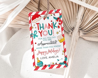 May include: A rectangular gift tag with a red and white striped border. The tag features the words "THANK YOU!" in colorful text, along with holiday-themed illustrations. The message "Happy Holidays!" and the name "AMELIA" are also included.