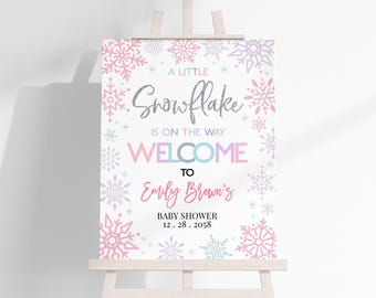 May include: A white welcome sign with a pink, blue, and purple snowflake design. The text reads "A Little Snowflake is on the Way Welcome to Emily Brown's Baby Shower 12.28.2058".