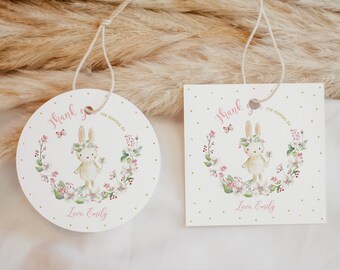 May include: Two thank you tags with a bunny rabbit wearing a flower crown and holding a flower. The tags are white with gold polka dots and pink flowers. The text on the tags reads "Thank you for coming" and "Love, Emily".