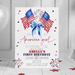 May include: A white invitation card with a patriotic theme. It features two American flags, a blue bow, and the text "Our American girl is turning one." The card includes details for Amelia's first birthday, with red and blue accents.