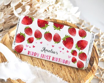 May include: A white chocolate bar wrapper with a strawberry pattern and the text "Amelia's Berry First Birthday".