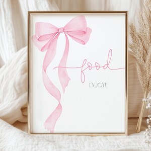 Op de afbeelding: Een printbaar bord met een roze aquarel strik en de tekst "food enjoy" in roze schrift.