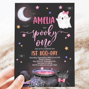 May include: A black and white invitation card with a pink and white ghost, a black cat, and a cauldron. The text on the card reads "Amelia is a spooky one. Join us to celebrate her 1st Boo-Day. Saturday, September 28th at 2:00 PM. Emily's House. Boo Drive & Donington Dr, San Jose, CA 95129. RSVP to Anne at 123-456-7890."