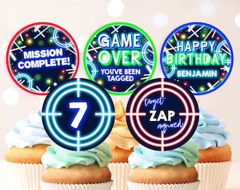 May include: Neon green, red, and blue cupcake toppers with a laser tag theme. The toppers feature phrases like "Mission Complete!" and "Game Over You've Been Tagged".