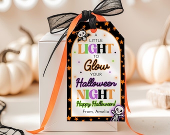 May include: A white gift box with a Halloween-themed tag. The tag has a black border with orange stars and the text "A LITTLE LIGHT TO Glow YOUR Halloween NIGHT Happy Halloween! From, Amelia." It is tied with a black and orange ribbon.