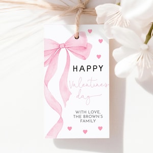 May include: A white gift tag featuring a pink watercolour bow and ribbons. The tag says "HAPPY Valentines day" with pink hearts. The text "WITH LOVE, THE BROWN'S FAMILY" is also included.