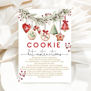 May include: A rectangular sign with the words "COOKIE kit instructions" in red and black. The sign features watercolor illustrations of Christmas cookies and greenery. Instructions for cookie decorating are printed below the title.