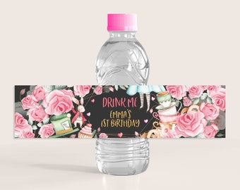 Könnte beinhalten: Wasserflaschenetikett mit schwarzem Hintergrund und goldenen Akzenten. Das Etikett zeigt ein rosafarbenes und weißes Blumenmuster mit einem weißen Kaninchen, einer Teetasse und einem Hut. Der Text auf dem Etikett lautet "Drink Me Emma's 1st Birthday".