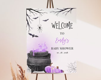May include: A Halloween-themed baby shower welcome sign on an easel. The sign features a cauldron with purple smoke, bats, spiders, and the text "Welcome to Emily's Baby Shower 10.28.2058."
